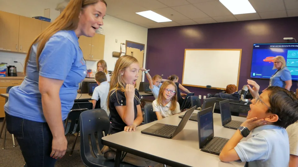 A teacher grins as her class reacts to the big screen.