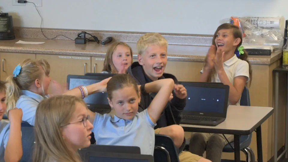Students cheer at their Chromebooks, arms in the air.